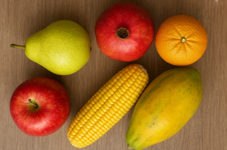 Fresh winter fruits (winter immunity boosters) including apple, pear, orange, papaya, pomegranate and corn placed on a wooden table — natural winter immunity booster foods.