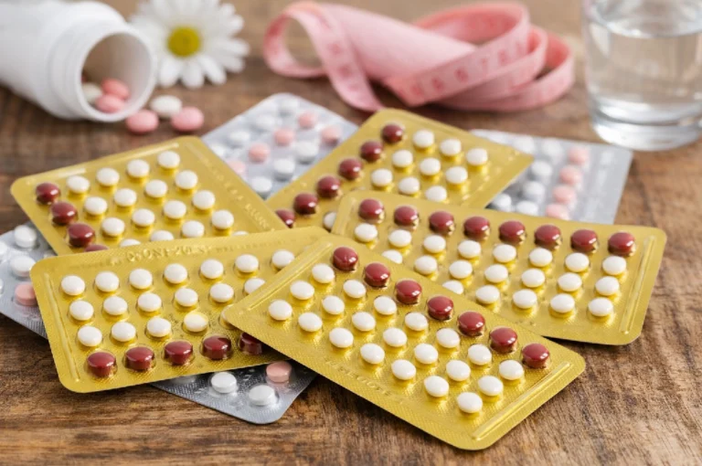 Close-up view of contraceptive blister packs showing yellow and silver birth control pills arranged on a wooden table, illustrating birth control pill side effects.