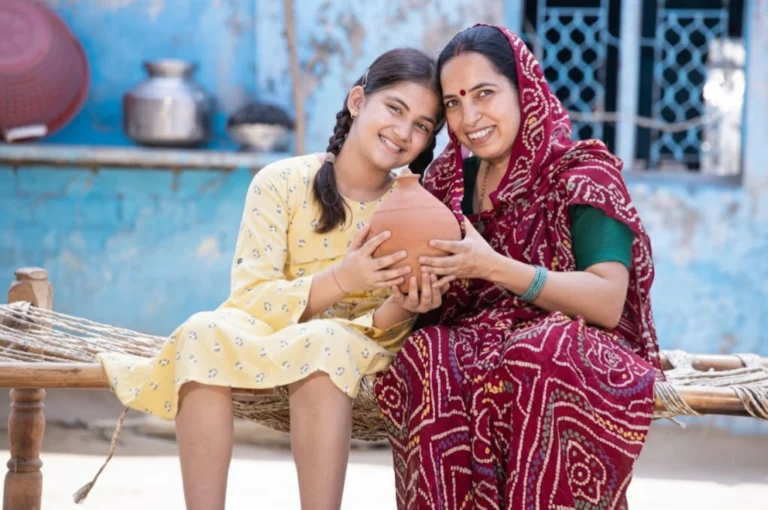 Mother and daughter smiling together while holding a clay pot, symbolizing savings and financial security under Sukanya Samriddhi Yojana.
